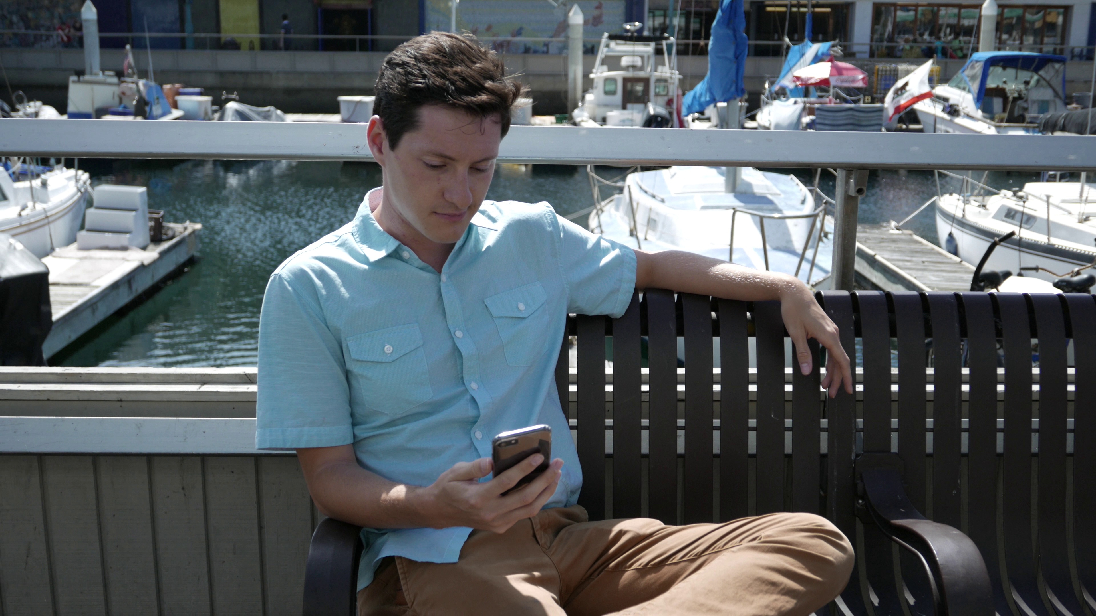 young-man-waiting-for-a-friend-on-a-bench-using-a-smartphone-SBI-349411465.jpg